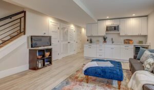 Modern living room with white kitchen cabinets, a staircase, and cozy furnishings.